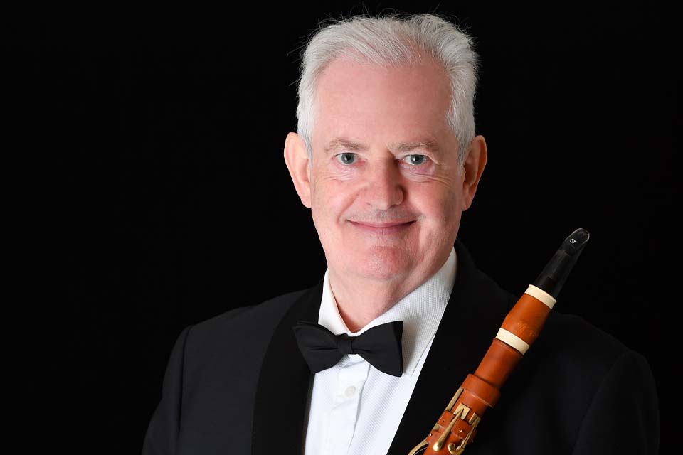 RCM Director Professor Colin Lawson stands in front of a dark background holding a clarinet.